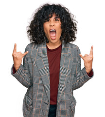 Young hispanic woman wearing business clothes shouting with crazy expression doing rock symbol with hands up. music star. heavy concept.