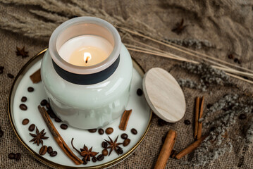 Aesthetic composition of candles, anise, cinnamon sticks and coffee beans on a background of burlap, decorated with dried flowers