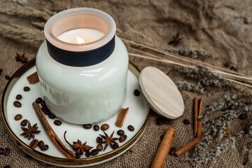 Aesthetic composition of candles, anise, cinnamon sticks and coffee beans on a background of burlap, decorated with dried flowers