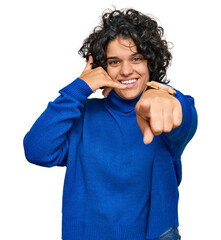 Young hispanic woman with curly hair wearing turtleneck sweater smiling doing talking on the...