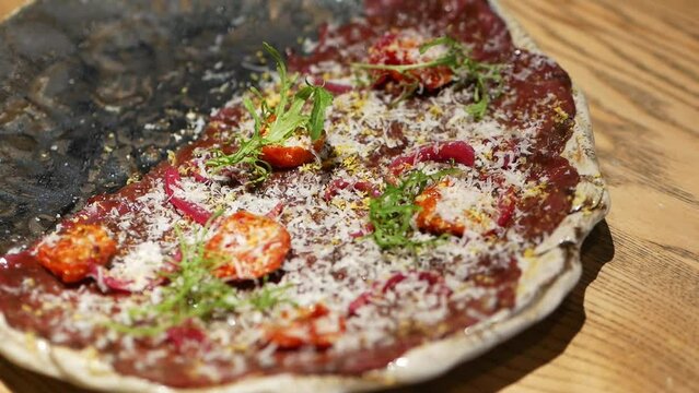 Beef carpaccio dish of thinly sliced pieces or slices of raw tenderloin meat with tomatoes, ruccula