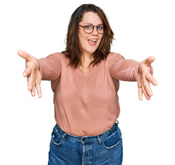 Young plus size woman wearing casual clothes and glasses looking at the camera smiling with open arms for hug. cheerful expression embracing happiness.