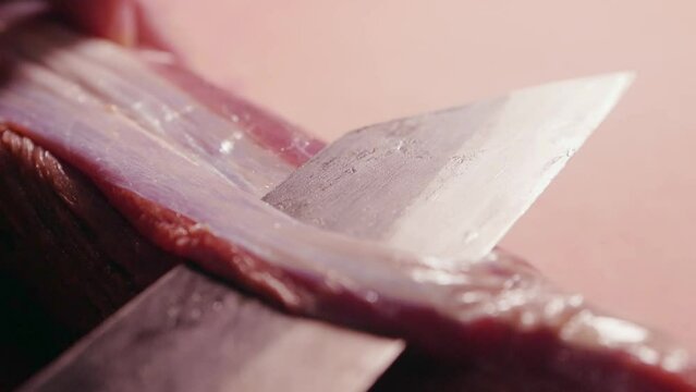 Chef cleans raw meat and cuts off connective tissue and surface membrane from a raw beef tenderloin