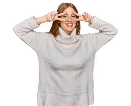 Young irish woman wearing casual winter sweater doing peace symbol with fingers over face, smiling cheerful showing victory