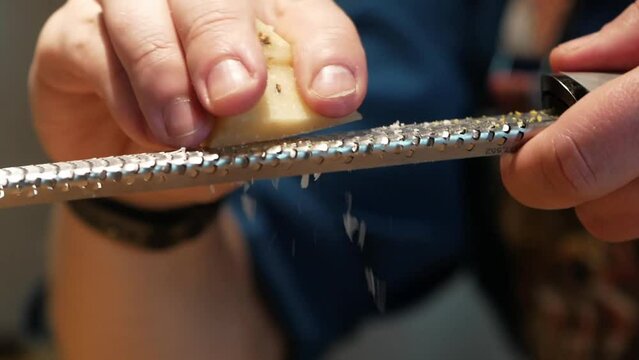Cheft grating parmesan cheese on a small fine metal grater