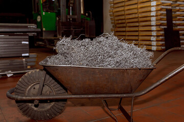 Metal shavings or scrap steel waste in a wheelbarrow at a factory. Metal shavings in the...