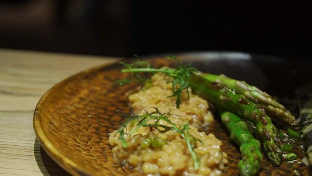 Chef decorating dish with green ruccula. Baked white fish dish with white sauce, bulgur, asparagus