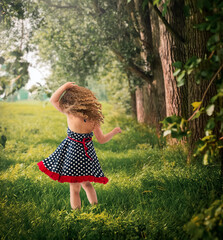 Back view little girl in polka dot dress wind blowing her curly hair walking in woods  - 549123467
