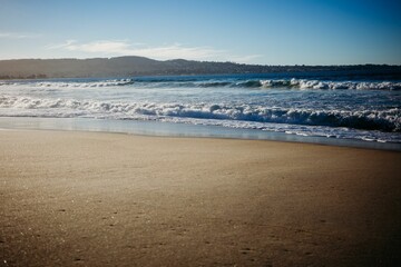 View of calm blue waves washing up on the smooth bronze-brown sand at a beach in San Francisco