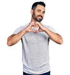 Young hispanic man with beard wearing casual grey t shirt smiling in love doing heart symbol shape with hands. romantic concept.