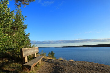 Romantic view over the Swedish lake called Malaren or M&auml;laren. Old wooden bench for relaxation. Blue sky and green nature. Copy space for text. J&auml;rf&auml;lla, Stockholm, Sweden, Scandinavia, Europe, 2021.