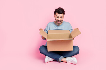 Full size photo of handsome young guy opening carton box excited peek inside dressed trendy blue...