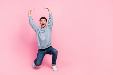 Full size photo of handsome young guy raise hands hold look heavy empty space dressed trendy blue clothes isolated on pink color background