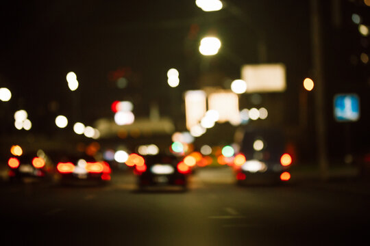 Night lights of big city background. The blurred cars moving on a road in traffic. Dark street bokeh with transport in the evening. Abstract photo of megapolis lifestyle. Urban highway in defocus.