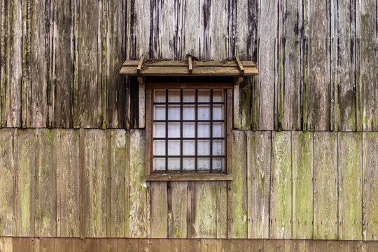 Closeup house window of an old wooden shack. Window seen in image has wooden lattice and small window roof.