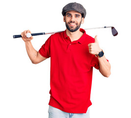Young handsome man with beard playing golf holding club and ball smiling happy and positive, thumb...