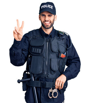 Young handsome man with beard wearing police uniform smiling with happy face winking at the camera doing victory sign. number two.