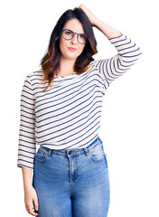 Fototapeta premium Beautiful young brunette woman wearing casual clothes and glasses confuse and wonder about question. uncertain with doubt, thinking with hand on head. pensive concept.