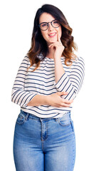 Fototapeta premium Beautiful young brunette woman wearing casual clothes and glasses looking confident at the camera with smile with crossed arms and hand raised on chin. thinking positive.