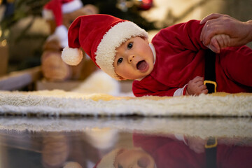 happy laughing baby in christmas outfit or santa claus dress crawling infront of xmas tree on a blanket on the floor in a cozy living room 