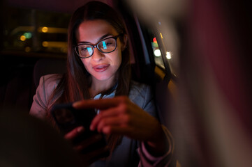 Business woman using smartphone while sitting in a backseat of a car at night
