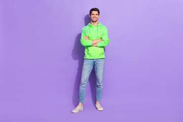 Full size photo of satisfied confident attractive guy dressed green hoodie denim jeans hands crossed isolated on violet color background