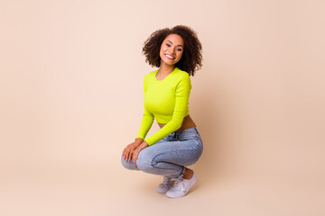 Full body photo of cute young lady curly hair squat crouch beaming smile dressed stylish yellow...
