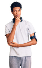 Young african american man wearing gym clothes and using headphones serious face thinking about question with hand on chin, thoughtful about confusing idea
