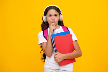 Thinking pensive clever teenager girl. Schoolgirl, teenage student girl in headphones hold books on yellow isolated studio background. School and music education concept. Back to school.