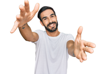 Young hispanic man wearing casual white t shirt looking at the camera smiling with open arms for hug. cheerful expression embracing happiness.