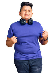 Little boy kid listening to music wearing headphones very happy and excited doing winner gesture with arms raised, smiling and screaming for success. celebration concept.