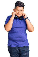 Little boy kid listening to music wearing headphones covering ears with fingers with annoyed expression for the noise of loud music. deaf concept.