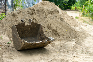 An excavator bucket near a pile of sand