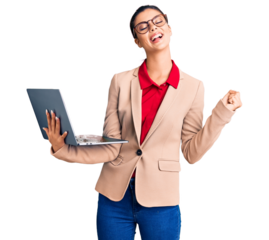 Young beautiful woman holding laptop screaming proud, celebrating victory and success very excited with raised arms