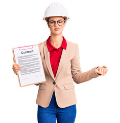 Young beautiful woman wearing architect hardhat holding clipboard with contract document annoyed and frustrated shouting with anger, yelling crazy with anger and hand raised