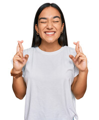 Young asian woman wearing casual white t shirt gesturing finger crossed smiling with hope and eyes...