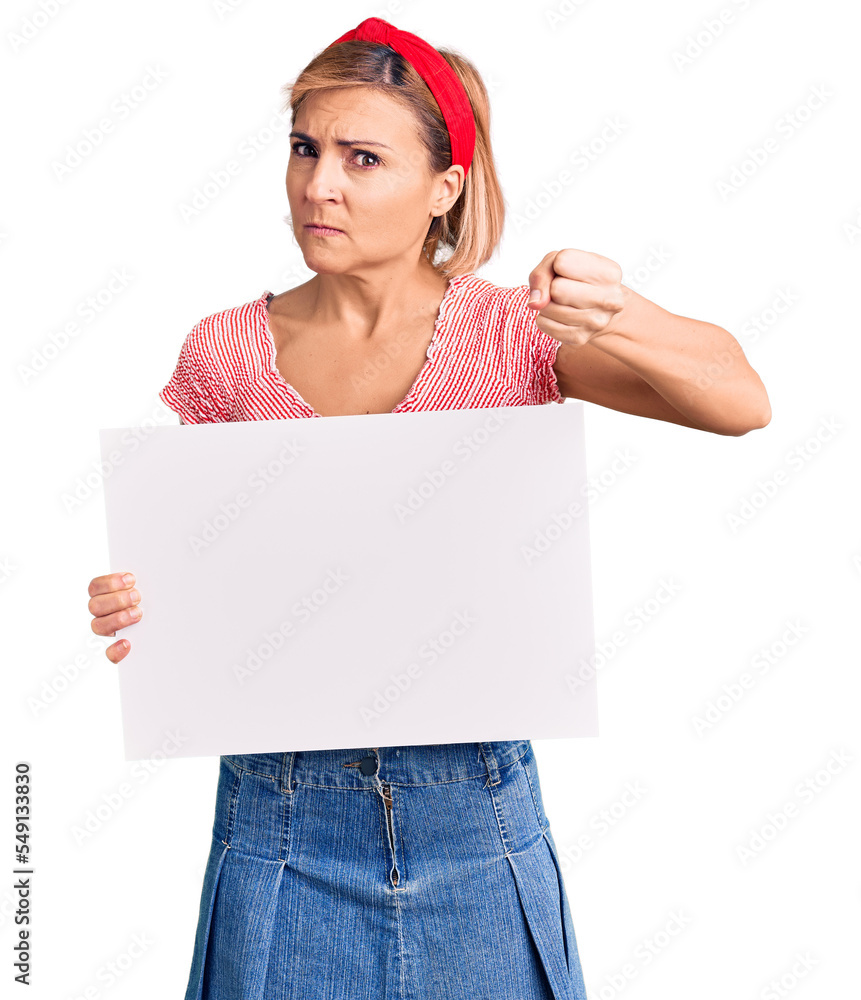 Poster young blonde woman holding blank empty banner annoyed and frustrated shouting with anger, yelling cr