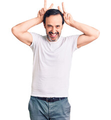 Middle age handsome man wearing casual t-shirt posing funny and crazy with fingers on head as bunny ears, smiling cheerful