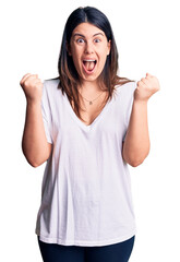 Young beautiful brunette woman wearing casual t-shirt celebrating surprised and amazed for success with arms raised and open eyes. winner concept.