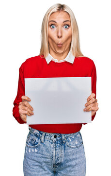 Young blonde woman holding blank empty banner scared and amazed with open mouth for surprise, disbelief face