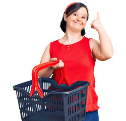 Brunette woman with down syndrome holding supermarket shopping basket surprised with an idea or...