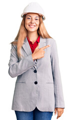 Beautiful young woman wearing architect hardhat cheerful with a smile of face pointing with hand and finger up to the side with happy and natural expression on face