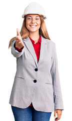 Beautiful young woman wearing architect hardhat smiling friendly offering handshake as greeting and welcoming. successful business.