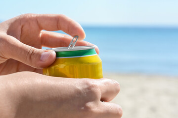 Woman opening can with sparkling drink at beach, closeup. Space for text