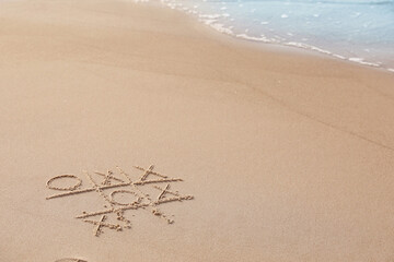 Tic tac toe game drawn on sand near sea, space for text