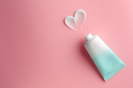 Tube and sample of facial cream on pink background, top view. Space for text