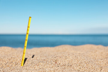 Fototapeta na wymiar Yellow weather thermometer in sand near sea, space for text