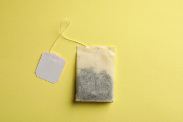 Paper tea bag with tag on yellow background, top view