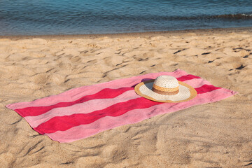 Beach towel and straw hat on sand near sea