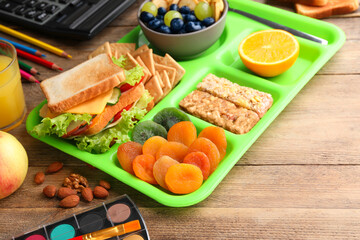 Serving tray of healthy food and stationery on wooden table. School lunch